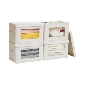 Four beige fabric storage boxes, ideal for a linen closet, are stacked in two rows—three hold folded clothes while one stores plush toys; one box lid is open and leans against the stack.