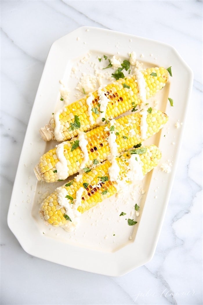 mexican corn on the cob on a white platter, on a marble surface.