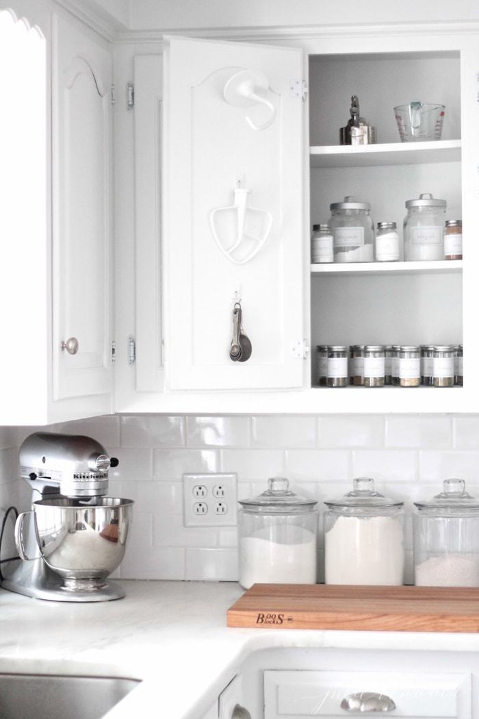 A white kitchen with a cabinet used for organized baking supplies.