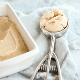 An ice cream scoop full of peanut butter ice cream, with a loaf of homemade frozen peanut butter ice cream recipe to the side.