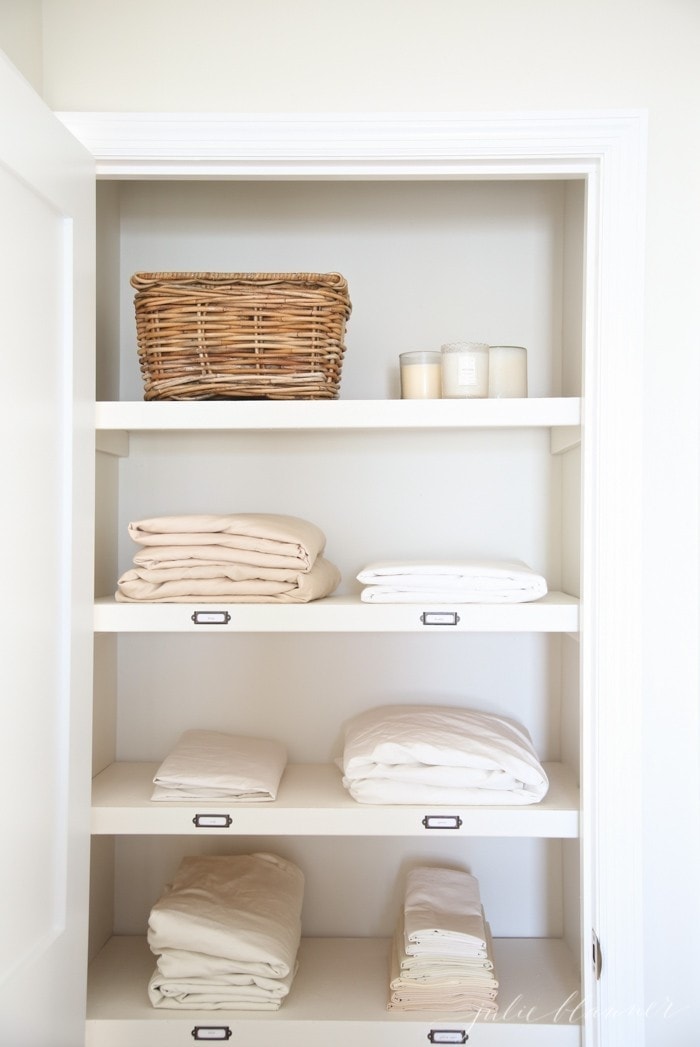 Looking into a white hall closet with white linens on the shelves.