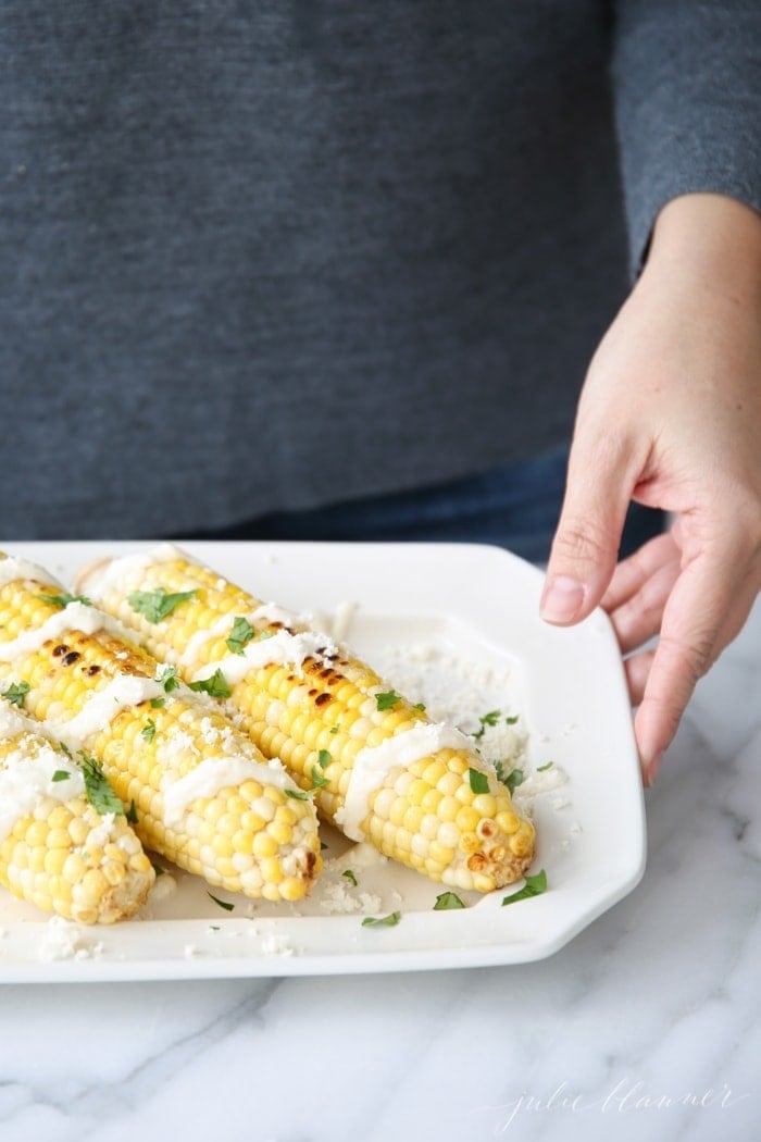 A woman in a gray shirt holding Mexican corn on the cob on a platter