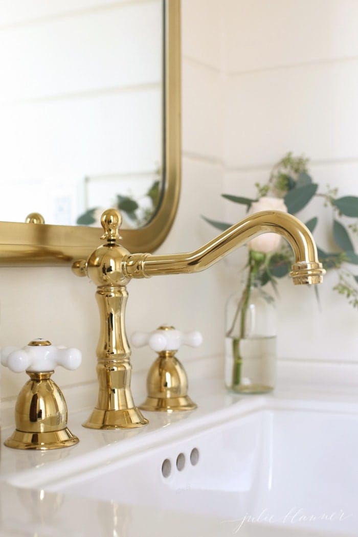 A powder room with a brass mirror and brass bathroom faucet