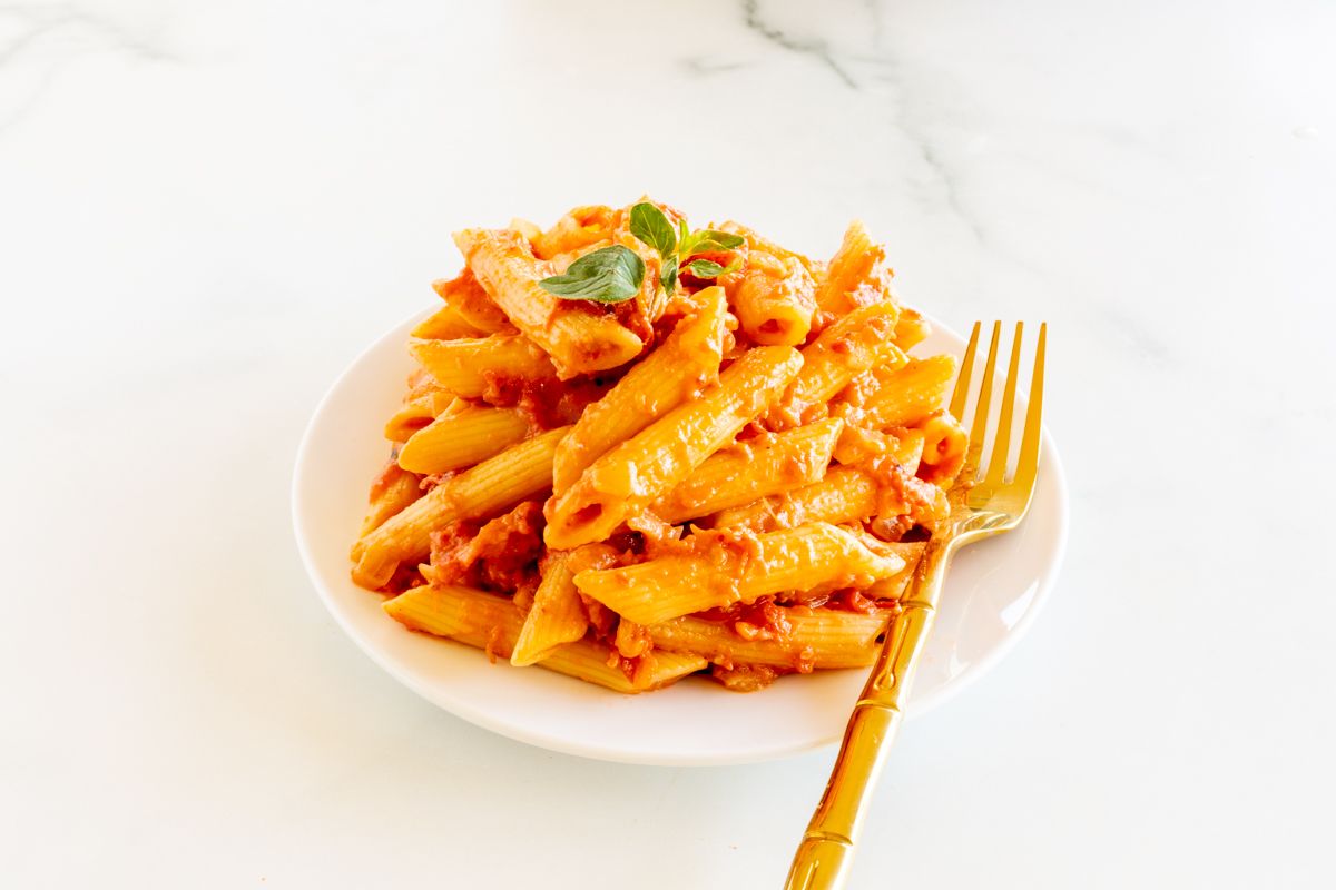 Penne alla vodka on a white plate with a gold fork.