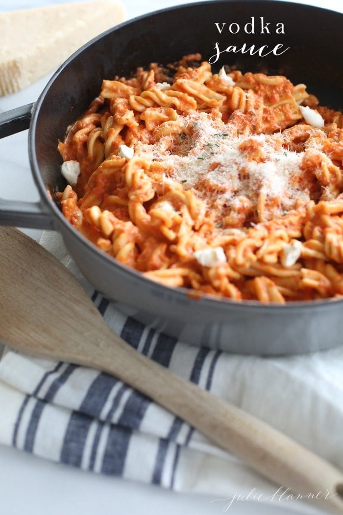 Pasta in a pan topped with parmesan, and a wooden spoon is to the side.