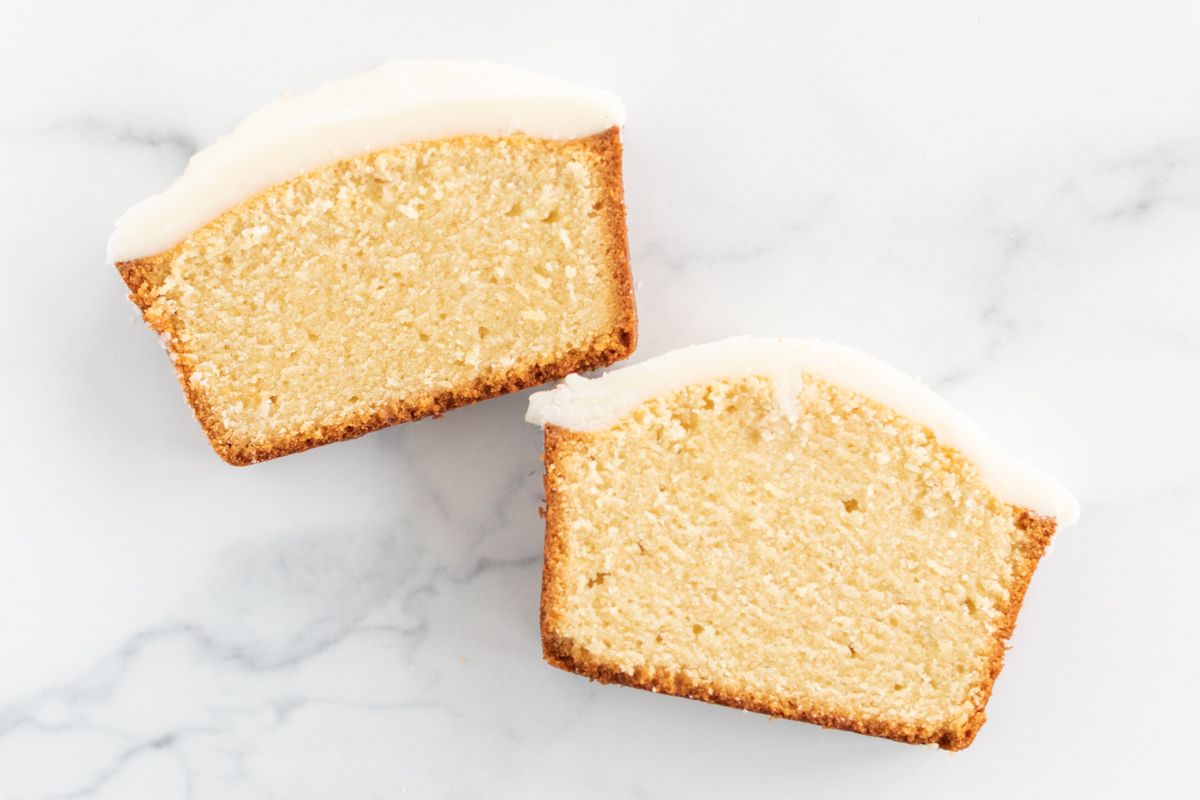 Two slices of an easy pound cake recipe with frosting on top, on a marble countertop. 