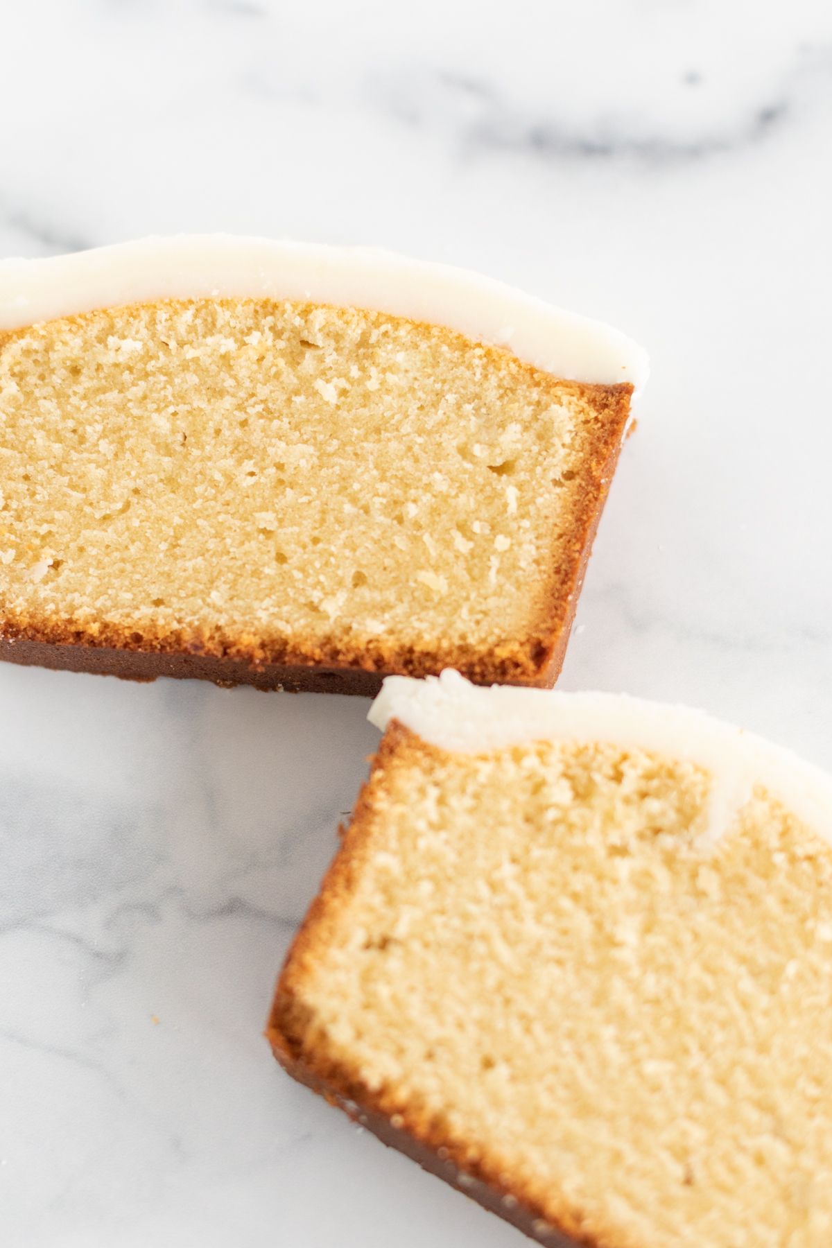 Two slices of an easy pound cake recipe with frosting on top, on a marble countertop.