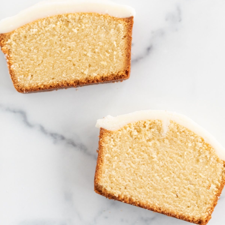 Two slices of an easy pound cake recipe with frosting on top, on a marble countertop.