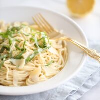 lemon basil pasta in white bowl with gold spoon and lemon in background