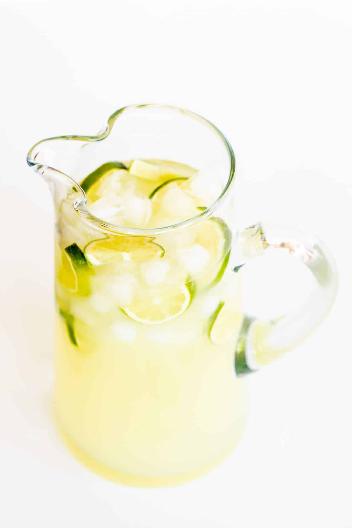 A clear glass pitcher full of homemade margaritas, sliced limes and ice.