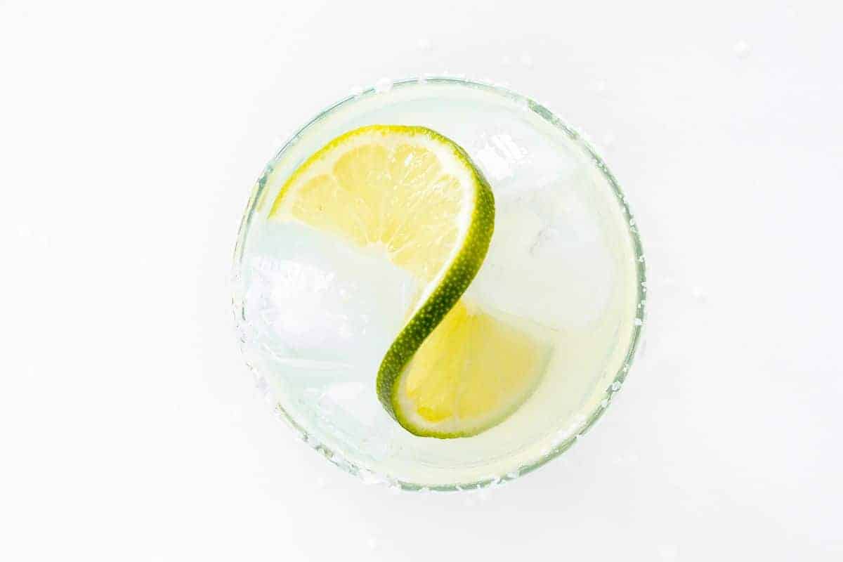 A clear glass with a homemade margarita, rimmed with salt and a slice of lime on a white background.