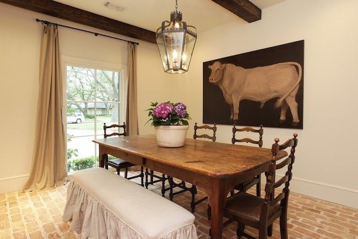 breakfast nook with cow painting, lantern, beams, brick floors, wood table