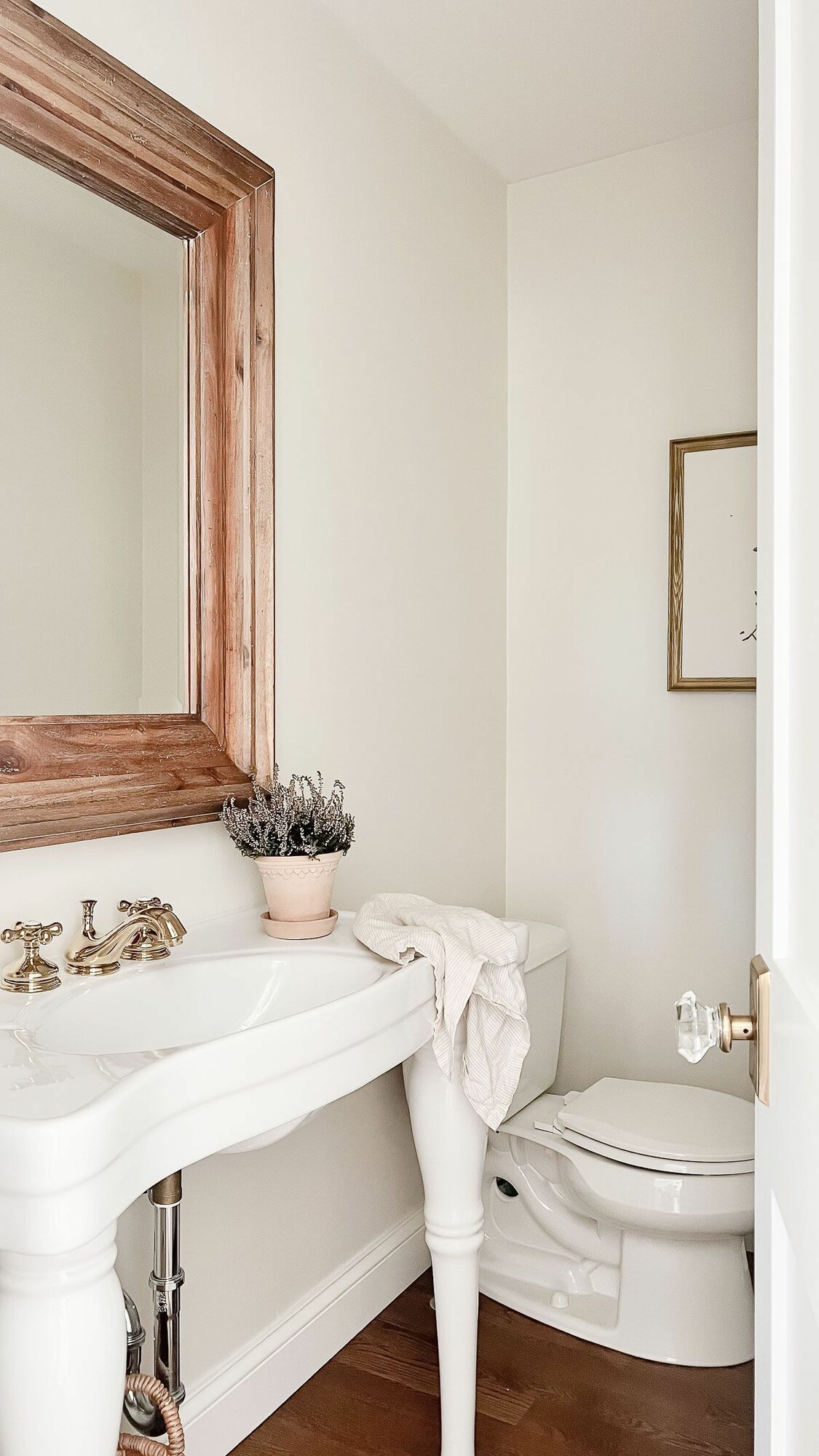 A guest bath with a wooden framed mirror and brass faucet.
