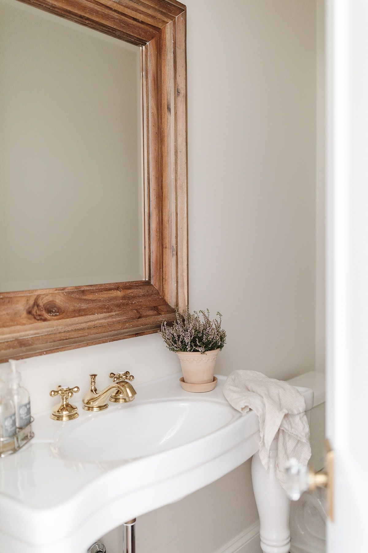 A guest bath with a wooden framed mirror and brass faucet.