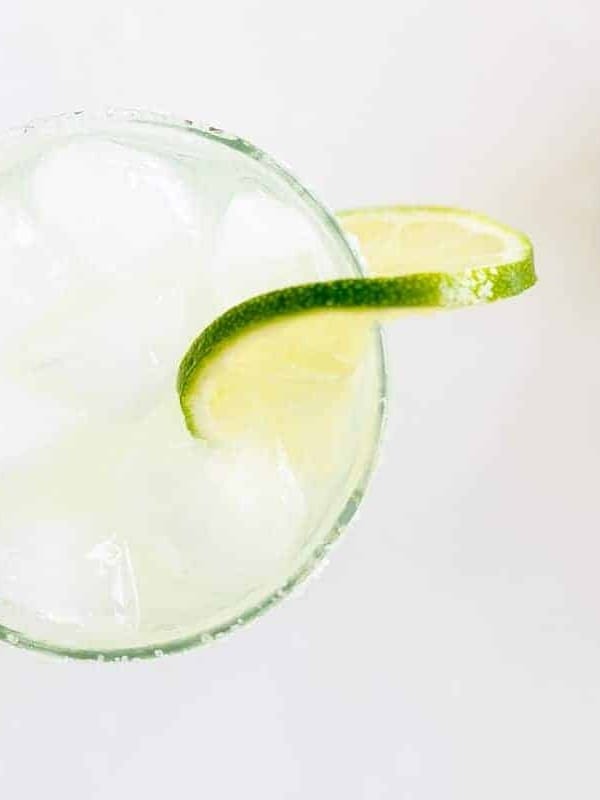 A clear glass with a homemade margarita, rimmed with salt and a slice of lime on a white background.
