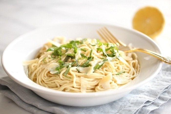 bowl of pasta topped with basil and parmesan lemon in the background
