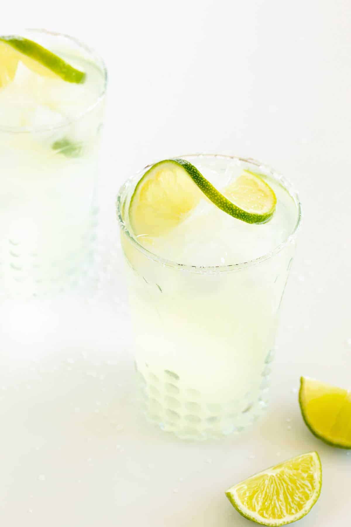 clear glasses full of a margarita from scratch, garnished with lime and lime wedges to the side.