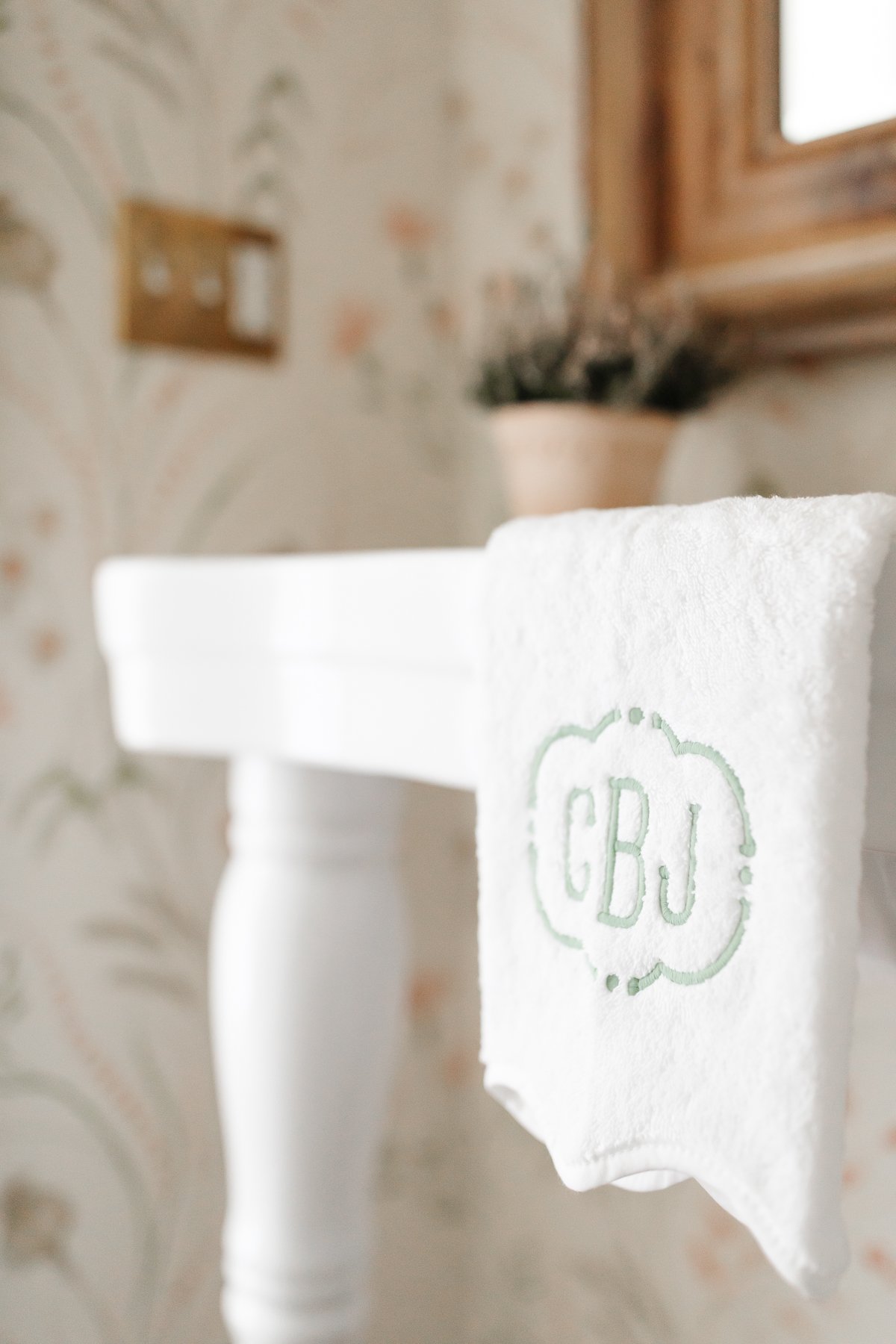 A white pedestal sink with an embroidered towel hanging over the edge
