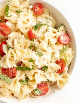 bow tie pasta salad in a bowl with cherry tomatoes basil and feta
