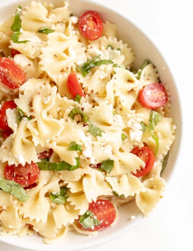 bow tie pasta salad in a bowl with cherry tomatoes basil and feta
