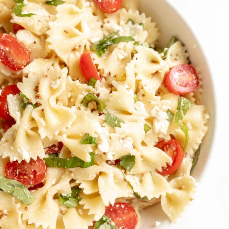 bow tie pasta salad in a bowl with cherry tomatoes basil and feta
