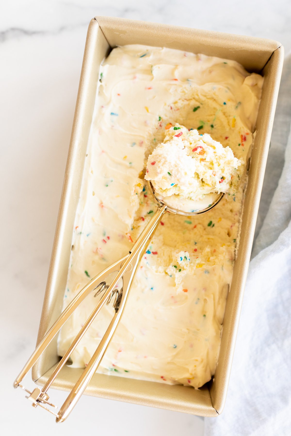 Homemade cake batter ice cream with rainbow sprinkles in a gold loaf pan.