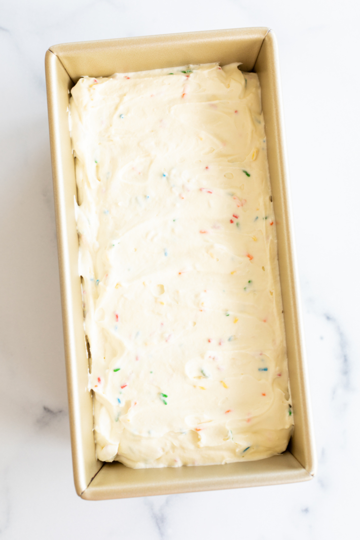Homemade cake batter ice cream with rainbow sprinkles in a gold loaf pan.