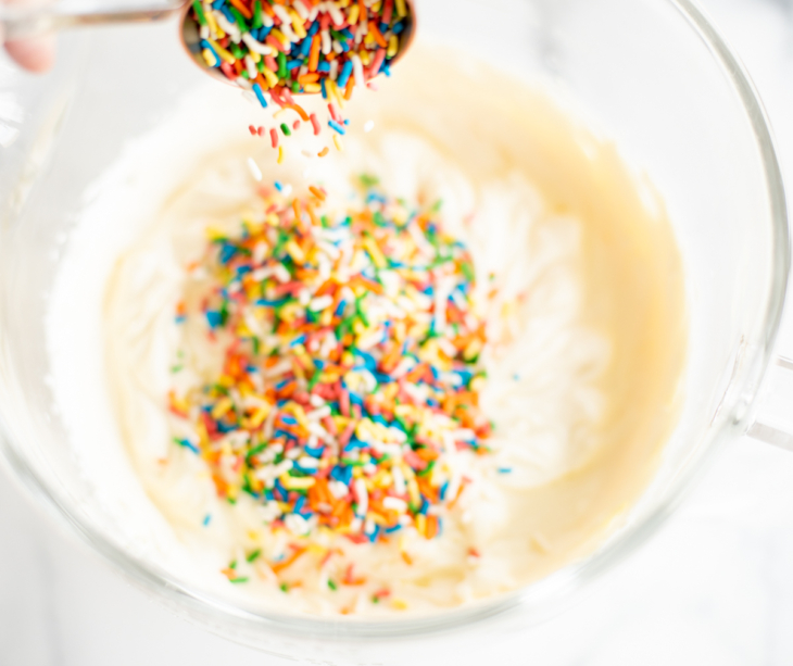 A close up of homemade cake batter ice cream, rainbow sprinkles being mixed into the batter.