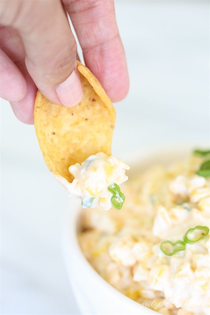 A hand dipping a chip into a white bowl full of corn dip.