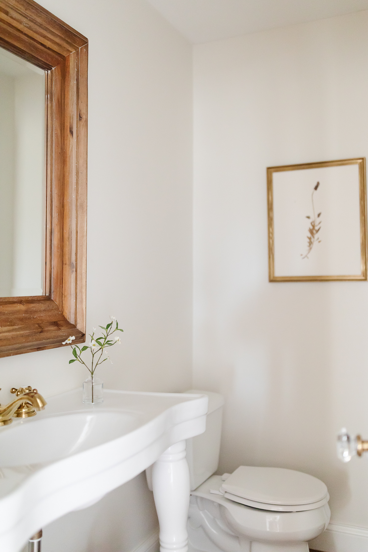 A white bathroom with a wooden vanity and mirror decorated with wall art.