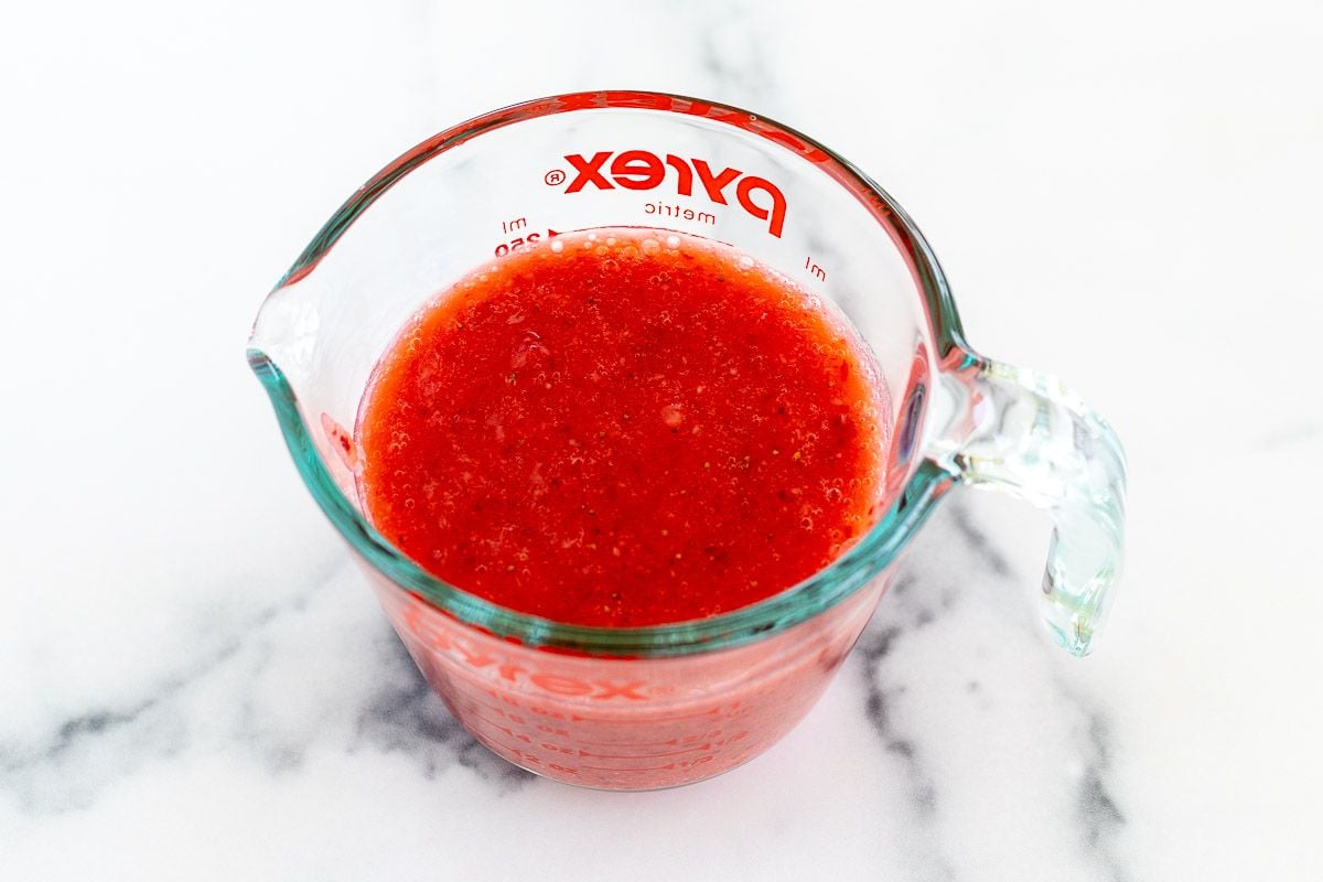 A glass pyrex measuring cup, full of strawberry puree
