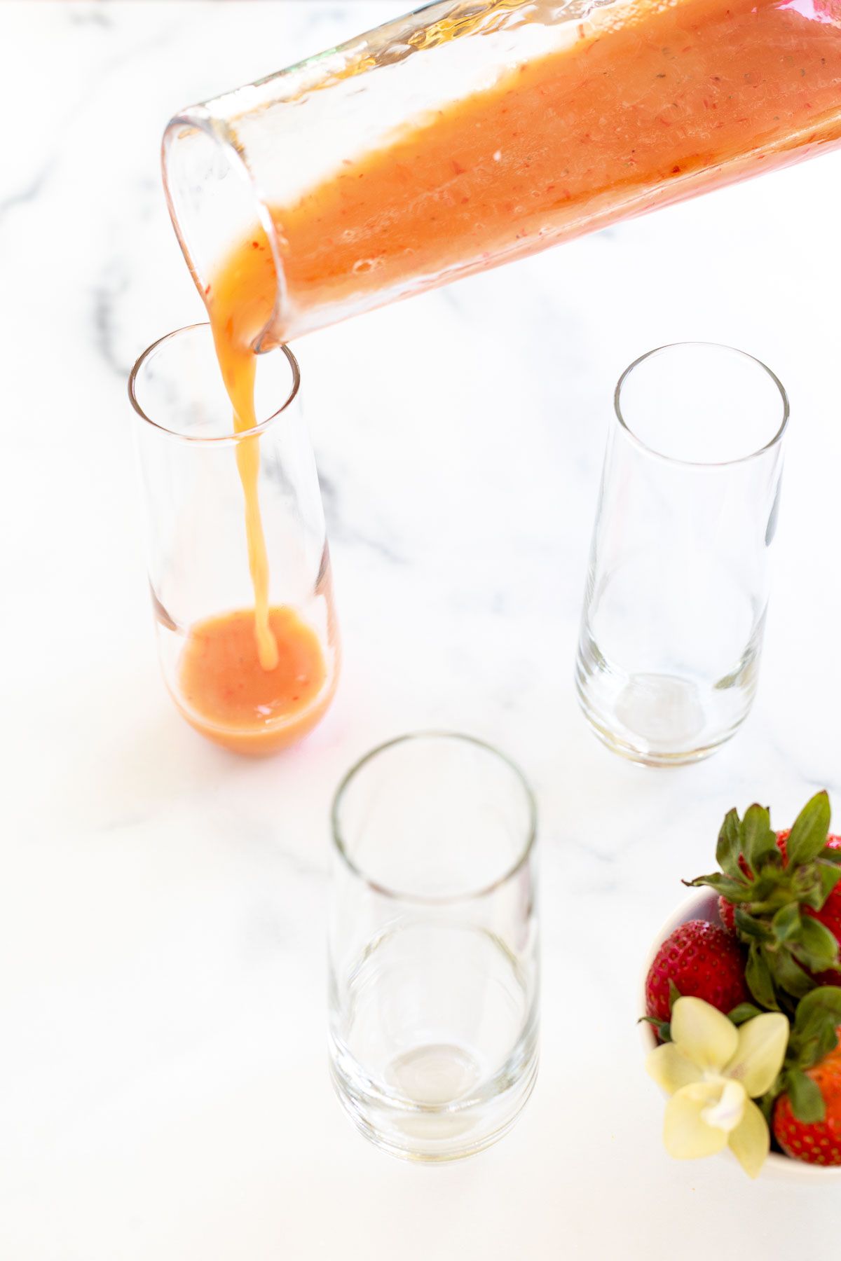 Strawberry puree pouring into a clear glass stemless champagne flute