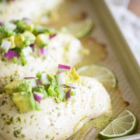 simple avocado salsa on top of chicken breasts on baking sheet with lime wedges