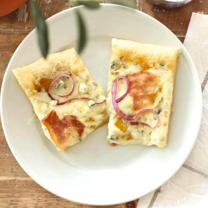pizza with prosciutto red onion and cheese on white plate