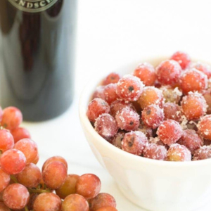 A bowl of sugared grapes next to frozen grapes and a bottle of wine.