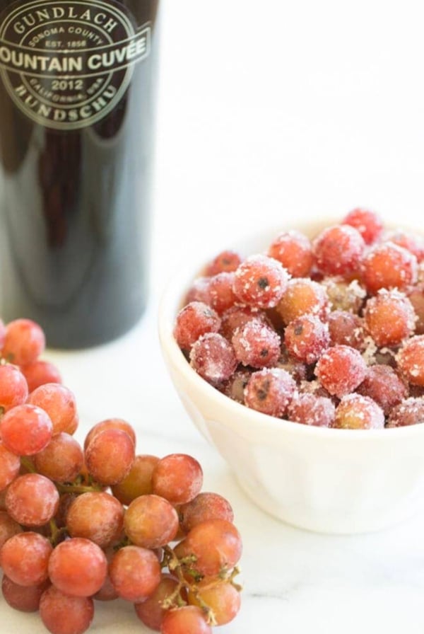 A bowl of sugared grapes next to frozen grapes and a bottle of wine.
