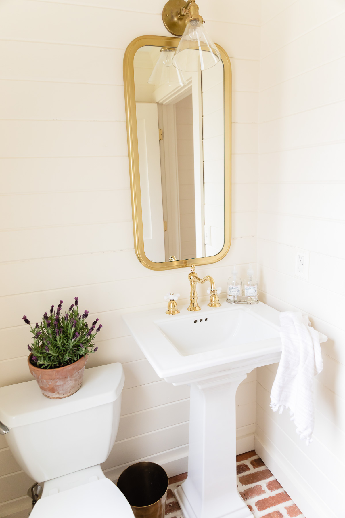 a white bathroom with brick floors and a brass faucet