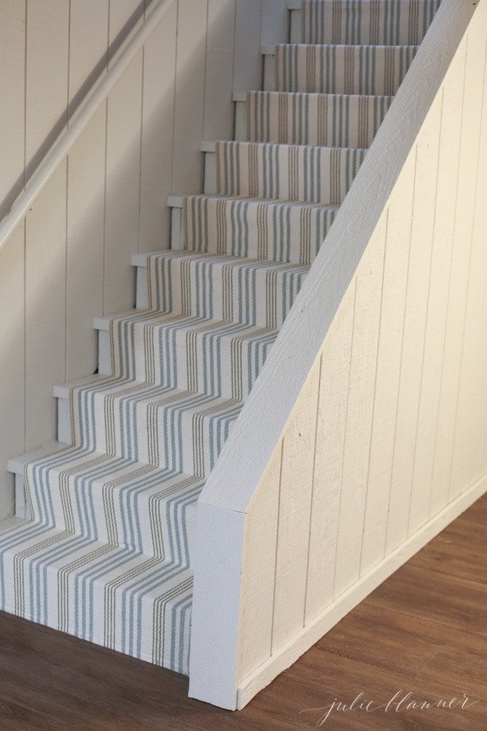 A striped stair runner coming down to a basement with neutral paint on the walls.