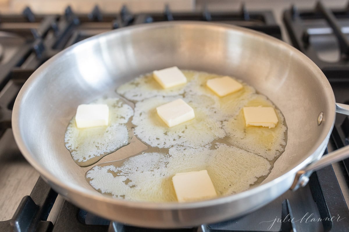 Chunks of butter melting in a silver stainless steel skillet.