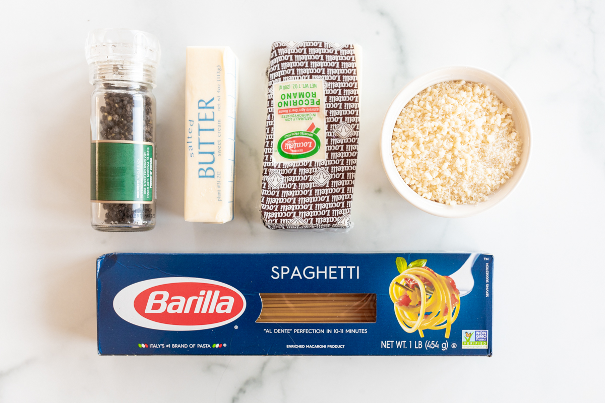 Ingredients for cacio e pepe laid out on a white marble countertop.
