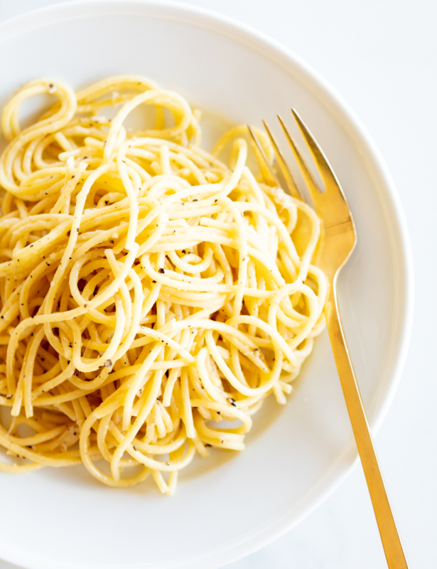 Cacio e pepe on a white plate with a gold fork.