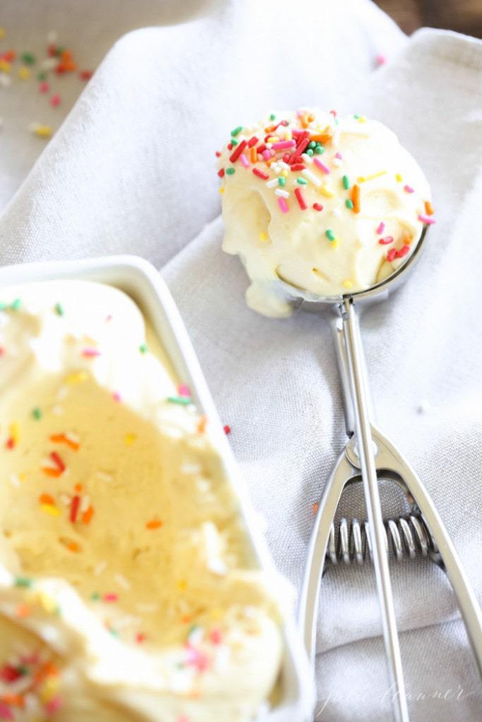 A white loaf pan filled with homemade ice cream, a scoop of ice cream covered in sprinkles to the side.