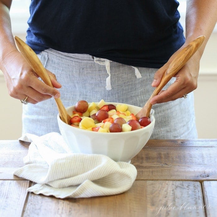 Fruit salad being mixed in a bowl with two wooden spoons