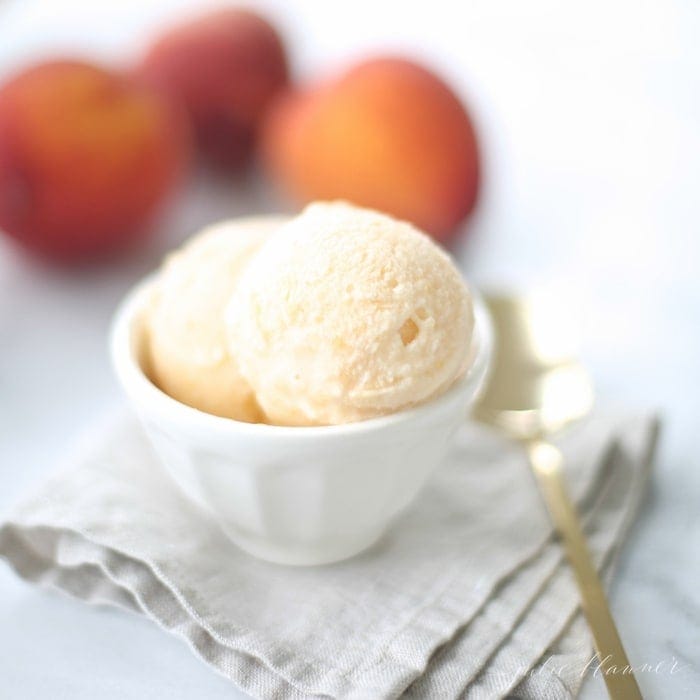 No churn peach ice cream in a white bowl with peaches and a gold spoon to the side. 