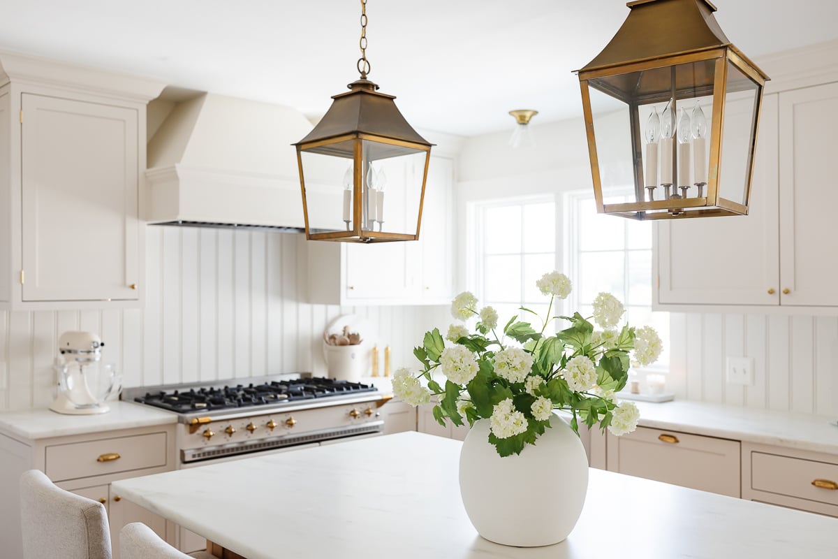 a white kitchen with brass lanterns over the island 