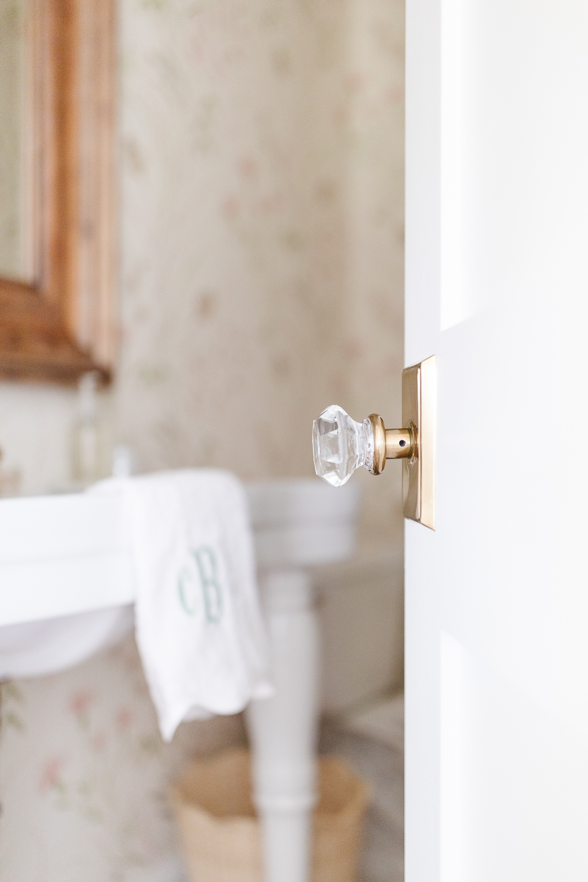 A white door with a brass and glass knob, looking into a wallpapered bathroom.