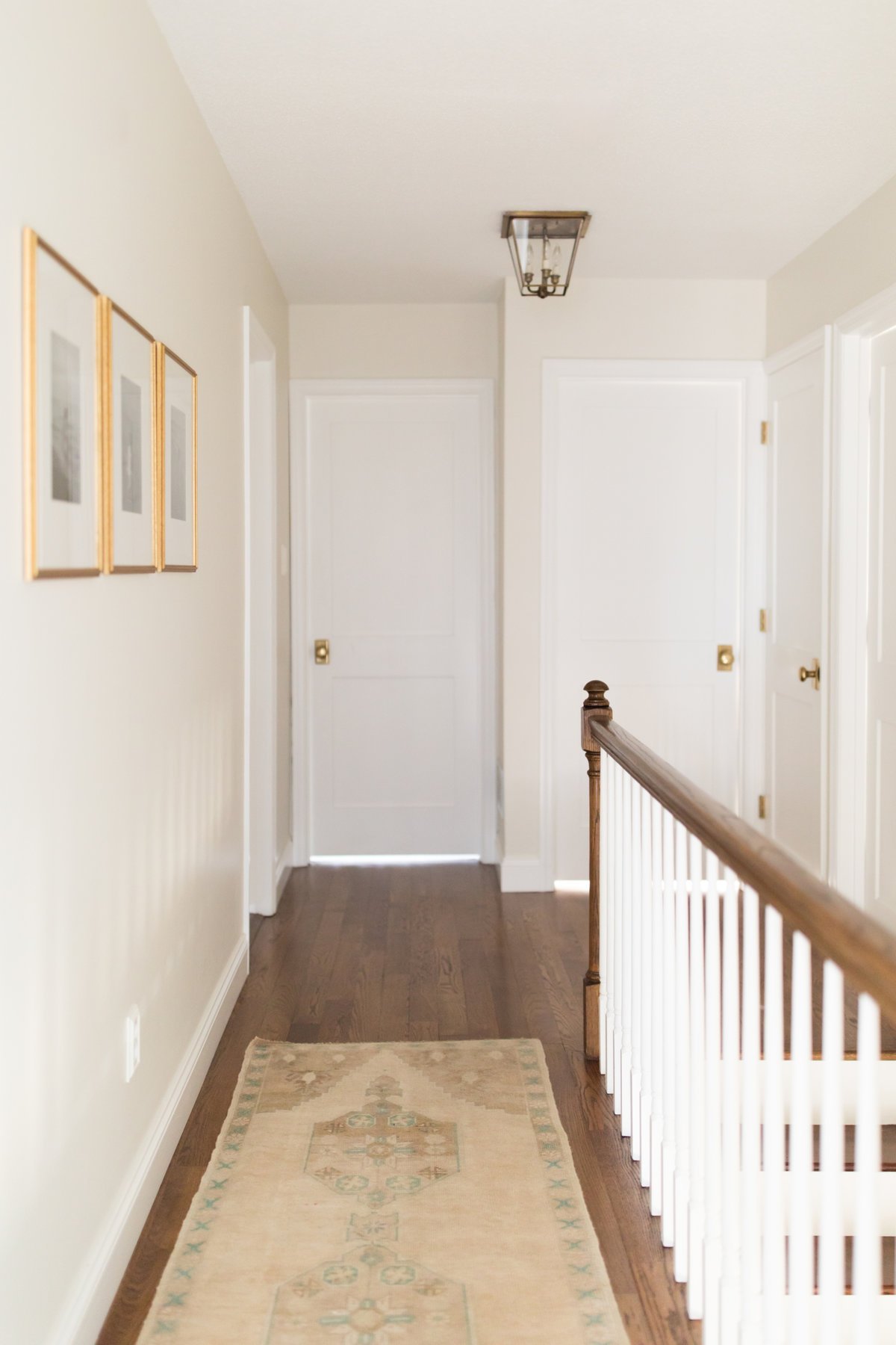 A white hallway with a vintage rug and brass light fixtures