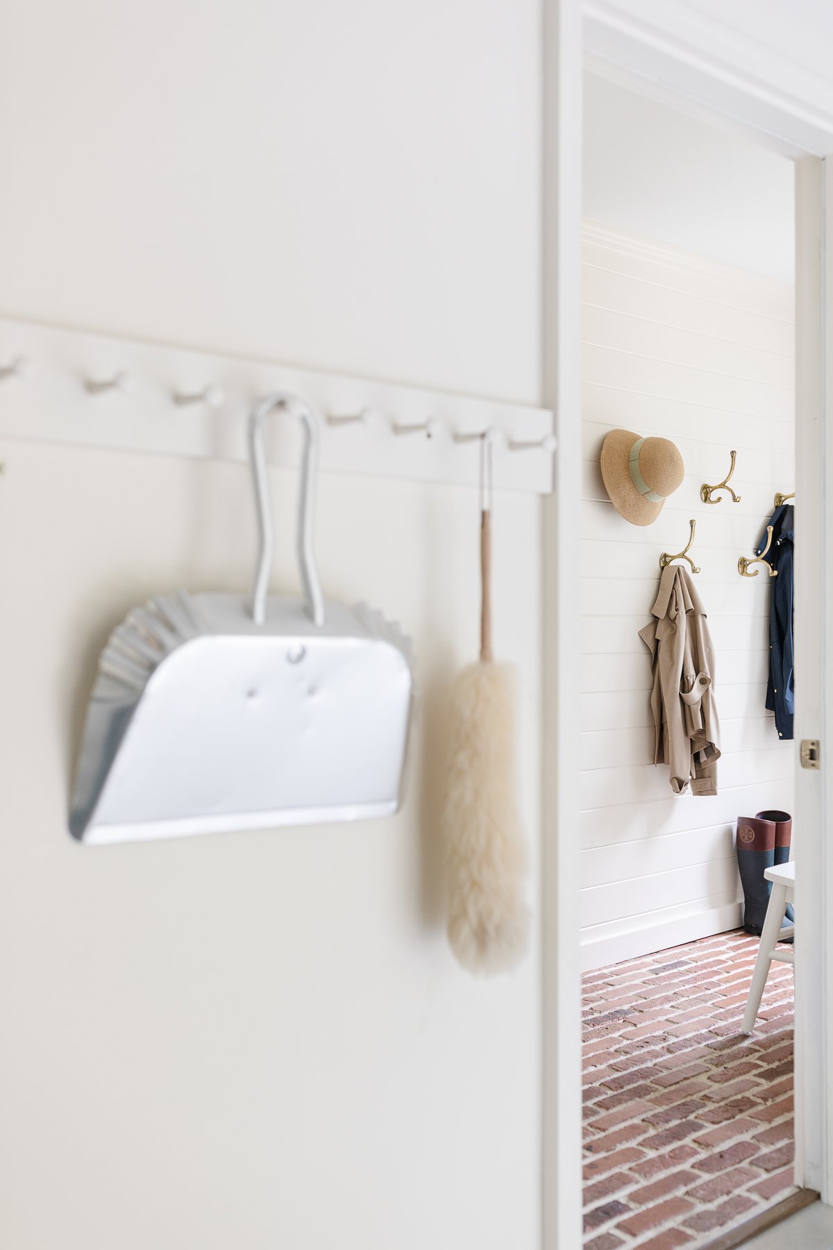 An organized peg rail in a mudroom with cleaning supplies