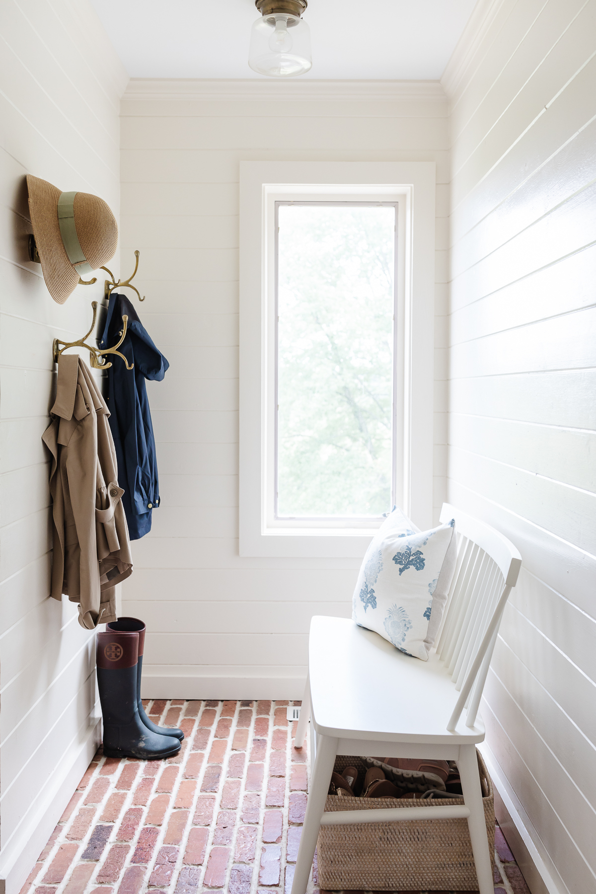 A mudroom with hooks and a white bench and brick floors in a guide to How to Sell a House Fast.