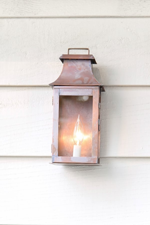 A small lantern providing outdoor lighting hangs on the side of a house.